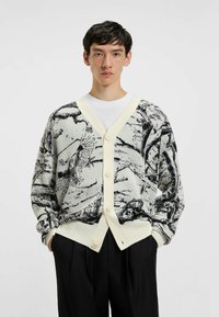 Strikket cardigan i creme med sorte abstrakte mønstre, V-hals design, fronter med knapper og løs pasform. Strukturstof med lange ærmer.