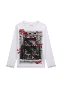 T-shirt bianca a maniche lunghe con una stampa grafica in bianco e nero di un edificio e testo rosso, con cuciture a contrasto lungo l'orlo.