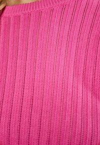 Maglione rosa a maglia con texture a costine, caratterizzato da righe verticali e colletto rotondo. Il materiale è leggero e morbido, con uno spessore medio.