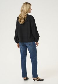 Blusa nera a maniche lunghe con una vestibilità comoda, abbinata a jeans azzurri a gamba dritta. Tacchi slingback neri completano l'outfit.