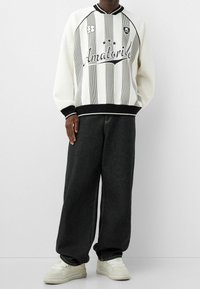 Sudadera de rayas blancas y negras con un corte oversize, puños acanalados, lettering bordado y pantalones anchos de mezclilla negra, combinados con zapatillas blancas.