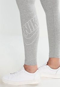 Grå leggings med en vit Nike-logotyp längs sidan, i kombination med vita sneakers. Leggings är åtsittande och tillverkade av mjukt material.