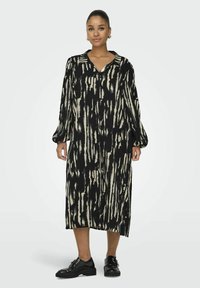 Robe à motifs noir et crème avec un col, des manches longues et une fermeture à boutons. Longueur genou, fabriquée dans un tissu léger avec une texture fluide.
