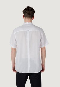 Camisa de manga corta, blanca, hecha de una tela ligera. Presenta un corte recto en la parte trasera con una costura central y una pequeña etiqueta cerca del cuello.