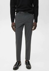 Grijze op maat gemaakte broek met een subtiele textuur, slim fit en een vlakke voorkant, gecombineerd met zwarte instappers en een zwarte trui.