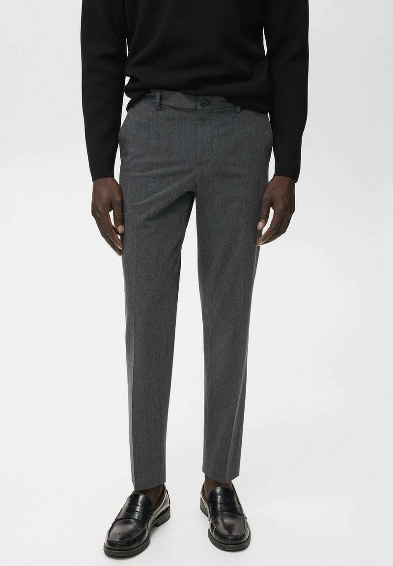 Grijze op maat gemaakte broek met een subtiele textuur, slim fit en een vlakke voorkant, gecombineerd met zwarte instappers en een zwarte trui.