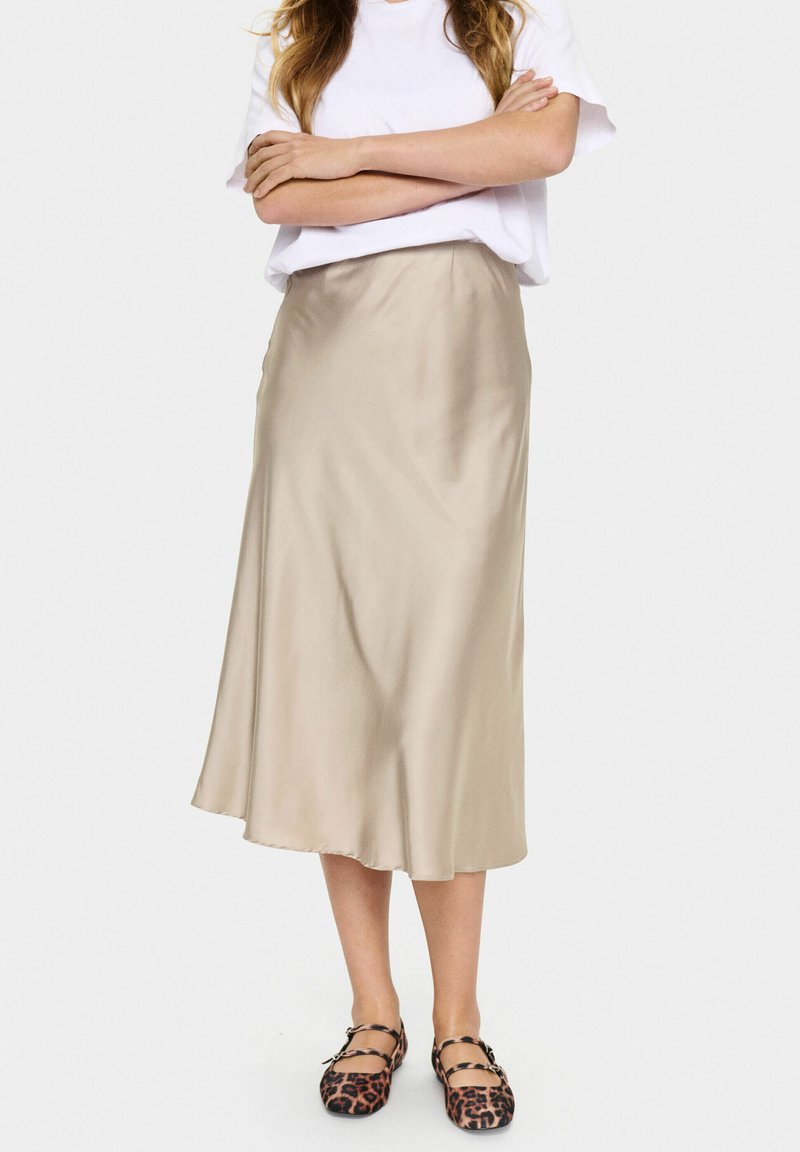 Beige satin midi skirt with a smooth texture, flared shape, and an elastic waistband, paired with black and brown leopard-print flats.