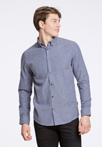 Niebieska koszula z długim rękawem, uszyta z fakturowanej tkaniny, z kołnierzykiem i zaokrąglonym dołem, z czarnymi guzikami.