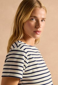 Kreemivärvi triibuline T-särk tumesiniste triipudega, lühikeste varrukatega ja ümmarguse kaelusega. Pehme kangas sileda tekstuuriga.