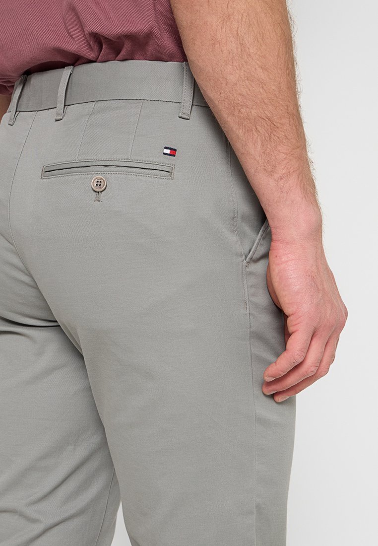 Helle graue Hose aus Baumwolle mit glatter Textur, ausgestattet mit einer Gesäßtasche und einem kleinen Logopatch. Detaillierte Nähte sind sichtbar.