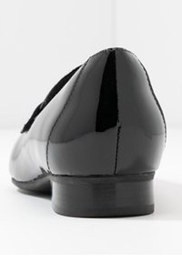 Chaussure en cuir verni noir avec un petit talon, un design élégant et une texture lisse. Vue de dos montrant un bout arrondi et des détails de couture subtils.