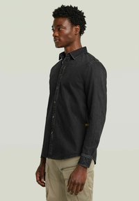 Camicia in denim nero con colletto a contrasto, tessuto strutturato e cuciture a contrasto. Presenta maniche lunghe e un discreto etichetta con logo all'orlo.