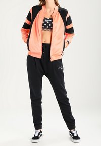 Růžovo-černá bomber bunda s pruhy, kombinovaná s crop topem s puntíky, černými tepláky a černými teniskami.