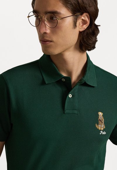 Camisa polo verde escuro com um acabamento texturado, apresentando um design de cão bordado e o texto "Polo" no lado esquerdo. Gola clássica e botões.