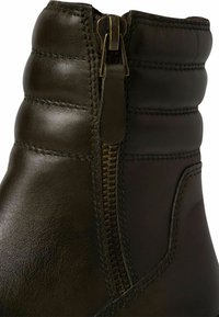 Botte de cheville en cuir vert foncé avec fermeture éclair sur le côté et texture matelassée près du haut. Fini lisse avec des détails de coutures visibles.