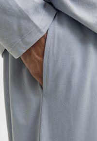 Hand resting inside the pocket of light blue soft fabric garment, showing detailed stitching and texture.