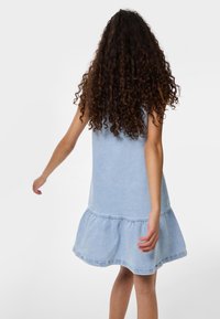 Ljusblå denimklänning med en åtsittande liv och en utsvängd, volangkant. Har en enkel ärmlös design och ett mjukt, texturerat tyg.