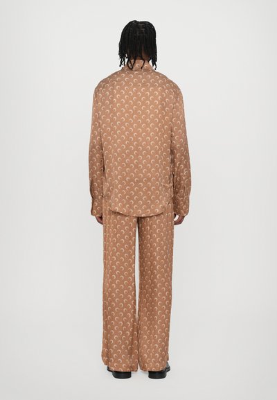 Satin shirt and pants set in tan with white crescent patterns. Loose fit, long sleeves, and wide-leg trousers.