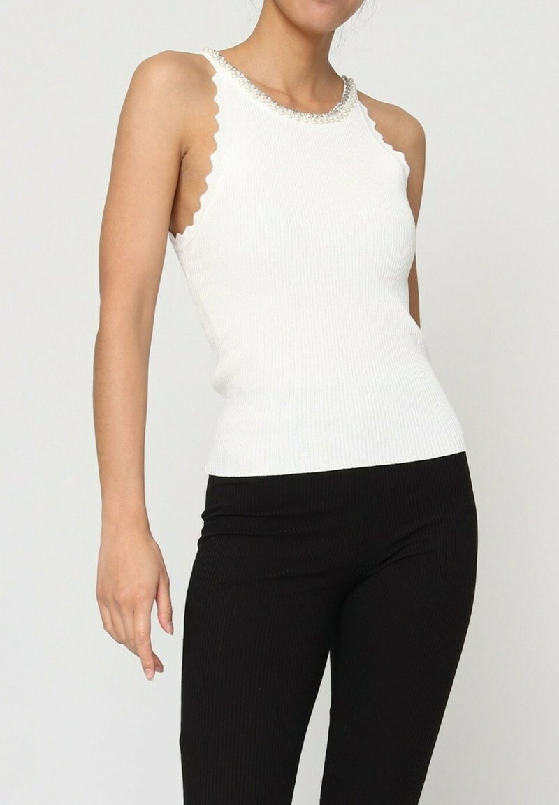 Débardeur blanc à côtes avec des bords festonnés et un col en perles, porté avec un pantalon noir ajusté. Mettez en avant la texture et la coupe ajustée.