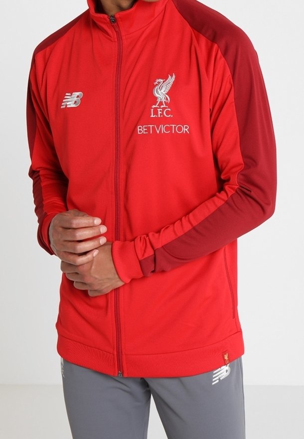 Rød zip-jakke med kontrastfarvede mørkerøde ærmer, der har Liverpool FC-logoet og "BETVICTOR" tekst i hvid. Glat stof med manchetter.