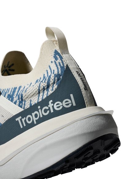 Arrière d'une basket Tropicfeel blanche et bleue avec tige tricotée, languette de tirage et semelle noire texturée sur fond blanc.