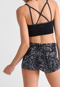 Czarny stanik sportowy z krzyżującymi się ramiączkami i małym logo Nike, w zestawie z czarno-białymi spodniami szortami z falistym wzorem.