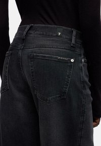 Zwarte denim jeans met achterzakken, een rechte pasvorm en een klein groen label met het nummer 7. Subtiele gestructureerde details langs de zakken.