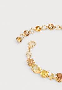 Gouden armband met verschillende gele en amberkleurige edelstenen in ronde en vierkante vormen, met een karabijnsluiting op een witte achtergrond.