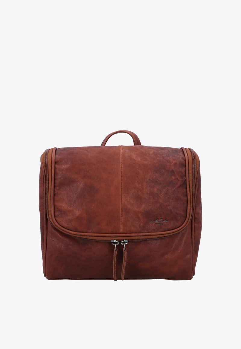 Bruine leren toilettas met dubbele ritssluiting, klep aan de voorkant en een klein handvat bovenop tegen een witte achtergrond.