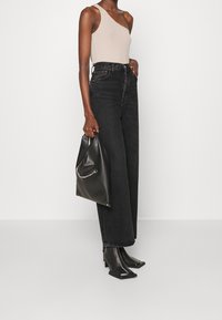 Asymmetriska beige ribbad bodysuit kombinerad med högmidjade svarta vida jeans och en svart handväska med kedjedetalj. Svarta klackade ankelskor.