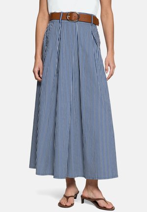 Femme portant une jupe longue à rayures verticales bleu et blanc avec plis, ceinture marron, haut blanc et sandales marron à talons.