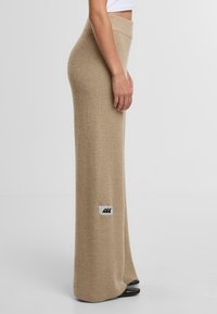Pletená béžová maxi sukně s vysokým pasem a texturovaným povrchem. Obsahuje malou logovou nášivku na boku.