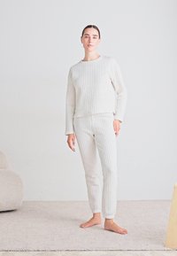 Ljust grått lounge-set i ribbad textur; långärmad topp och slim-fit byxor, båda med vertikala ränder. Enkelt mönster, mjukt material.