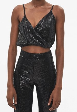 Czarny krótki top bez rękawów z cienkimi ramiączkami oraz dopasowane, wysokiej talii spodnie z cekinami na osobie ze swobodnie opuszczonymi ramionami.