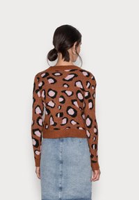 Brązowy sweter dziergany z czarno-różowym nadrukiem w panterkę, okrągłym dekoltem, krótki, z prążkowanym dołem, noszony z dżinsową spódnicą.