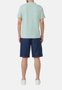 Jasnozielona bawełniana koszulka z krótkim rękawem w połączeniu z ciemnoniebieskimi szortami dżinsowymi. Uzupełniona białymi sneakersami. Widok z tyłu na zestaw.