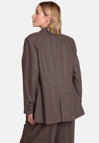 Brun rutete blazer med en strukturert design, som har høy krage, enkelt vent, og fire svarte knappeaksenter på ermene.