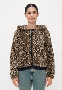 Leopardmønstret hettegenser med glidelås i myk, teksturert, brun og svart kunstpels, med hette og ribbestrikkede mansjetter og kant. Kombinert med lyseblå jeans.
