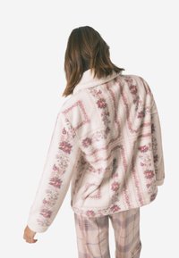 Fleecejacka med blommönster i rosa och krämfärger, med krage, avslappnad passform och långa ärmar. Mönstren visar på fina blommor.