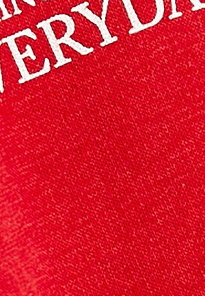 Punainen kangas, jossa on tekstuuri, esittää suurta valkoista tekstiä, joka lukee "JOKAPÄIVÄ." Ei muita kuvioita tai korostuksia.