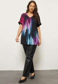 Tunica nera e colorata con una sfumatura, a maniche corte, caratterizzata da motivi viola, blu e turchese, abbinata a leggings neri lucidi e ballerine.