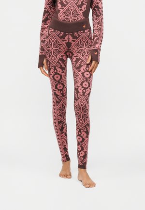 Primer plano de una persona que lleva leggings de talle alto con un patrón geométrico rosa y marrón y una camiseta de manga larga a juego. Descalzo.