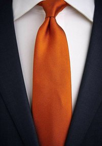 Orange texturerat slips med ett subtilt mönster, placerad mot en vit skjorta och en mörkblå kavaj, vilket framhäver en formell look.