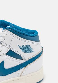 Bele superge z modrimi usnjastimi detajli in mrežasto podlogo. Ponaša se z logotipom Air Jordan na strani in teksturiranim podplatom. Zavezovanje na vezalke.