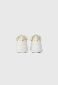 Hvite sneakers med en tykk såle, som har en glatt gullaccent på hælen og et preget merke på baksiden. Slitesterkt lærmateriale.