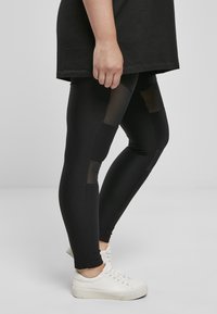 Leggings noires côtelées avec des accents en maille transparente ; associés à des baskets blanches et un haut noir surdimensionné. Tissu texturé avec une coupe ajustée.