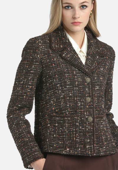 Tweed takki tummanruskeana monivärisillä langoilla, jossa on viilto-ommelkaulus, nappisulku ja kaksi etutaskua. Rakenne on tekstuurinen.
