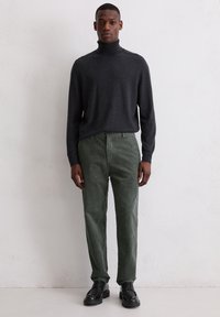 Donkergrijze coltrui gecombineerd met groene gestreepte corduroy broek. Zwarte veterschoenen maken de outfit compleet.