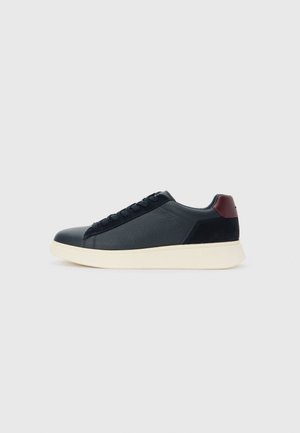 Low-top men's sneaker in black leather and suede with maroon heel tab and white rubber sole, viewed from the outer side.