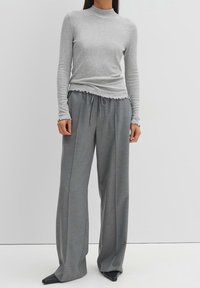 Grå långärmad topp med ståkrage och volangkant, ihopparad med lösa, högmidjade grå byxor som har dragsko och vida ben.